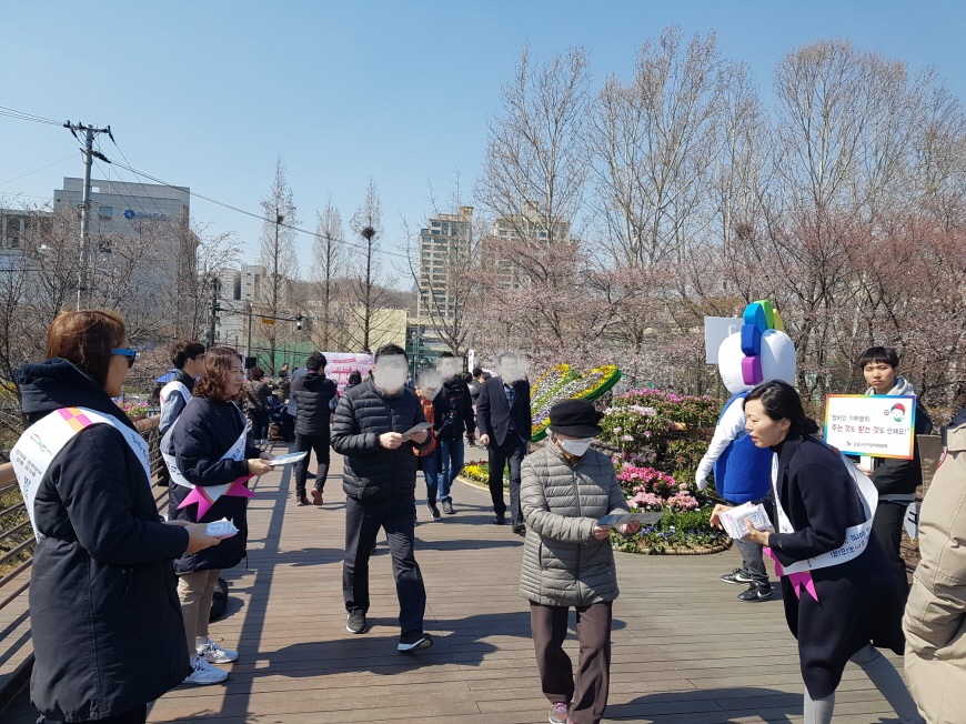 강남구선거관리위원회 직원들이 양재천 밀미리다리 위에서 어깨띠를 하고 피켓을 들어 축제방문객들에게 리플릿과 홍보용품을 배부하면서 기부행위 상시제한 안내 홍보 캠페인을 전개하고 있는 장면