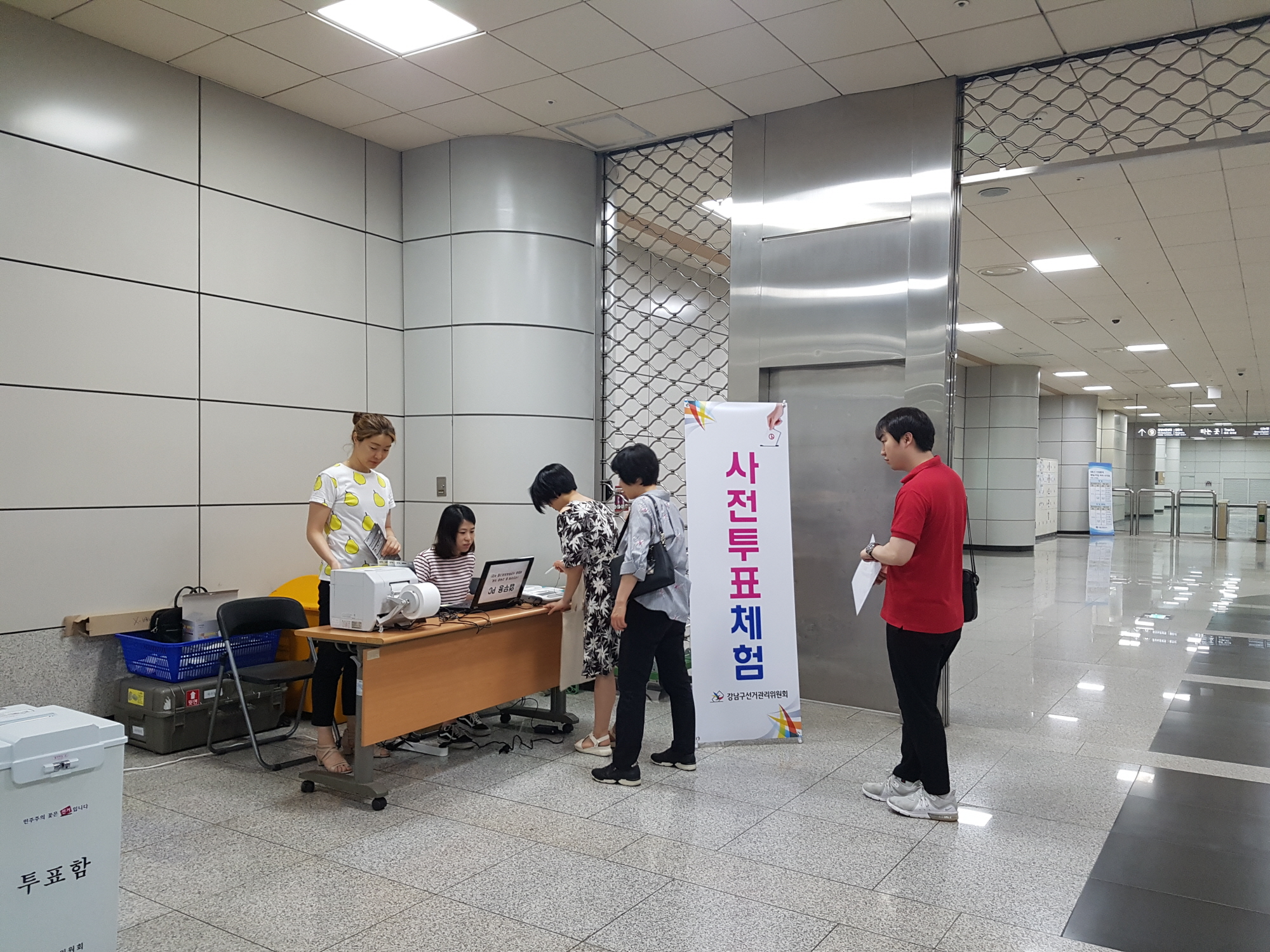 강남구선거관리위원회 직원 2명이 사전투표체험용 투표용지를 발급하고 일반시민 3명이 체험용투표용지를 받기위해 줄을 서서 기다리고 있는 장면