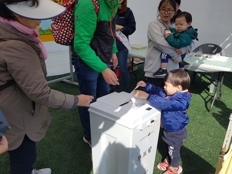 투표함에 투표용지를 넣는 아이와 가족의 모습